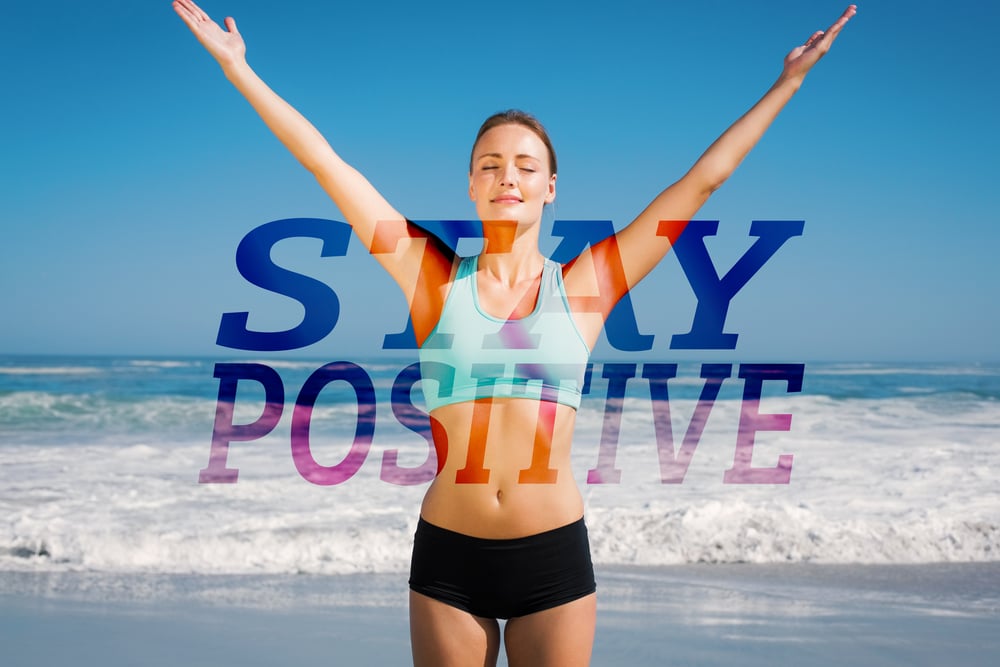 Fit woman standing on the beach with arms up against stay positive