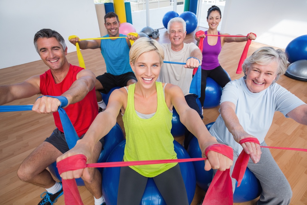 Portrait of happy men and women on fitness balls exercising with resistance bands in gym class-2